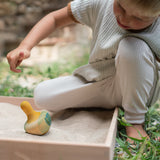 Kind spielt mit Holzkreisel Flowing Yellow Bird von Grapat in Sandkasten