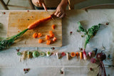 Kind schneidet Möhre vor handbemalten Veggies-Holzfiguren von Grapat