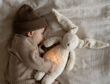 Baby mit Moonie Einschlafhilfe und Kuscheltier-Hase im Farbton Organic Sand